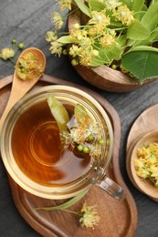 Photo of Tasty linden tea in cup, spoon, leaves and flowers on dark textured table, flat lay