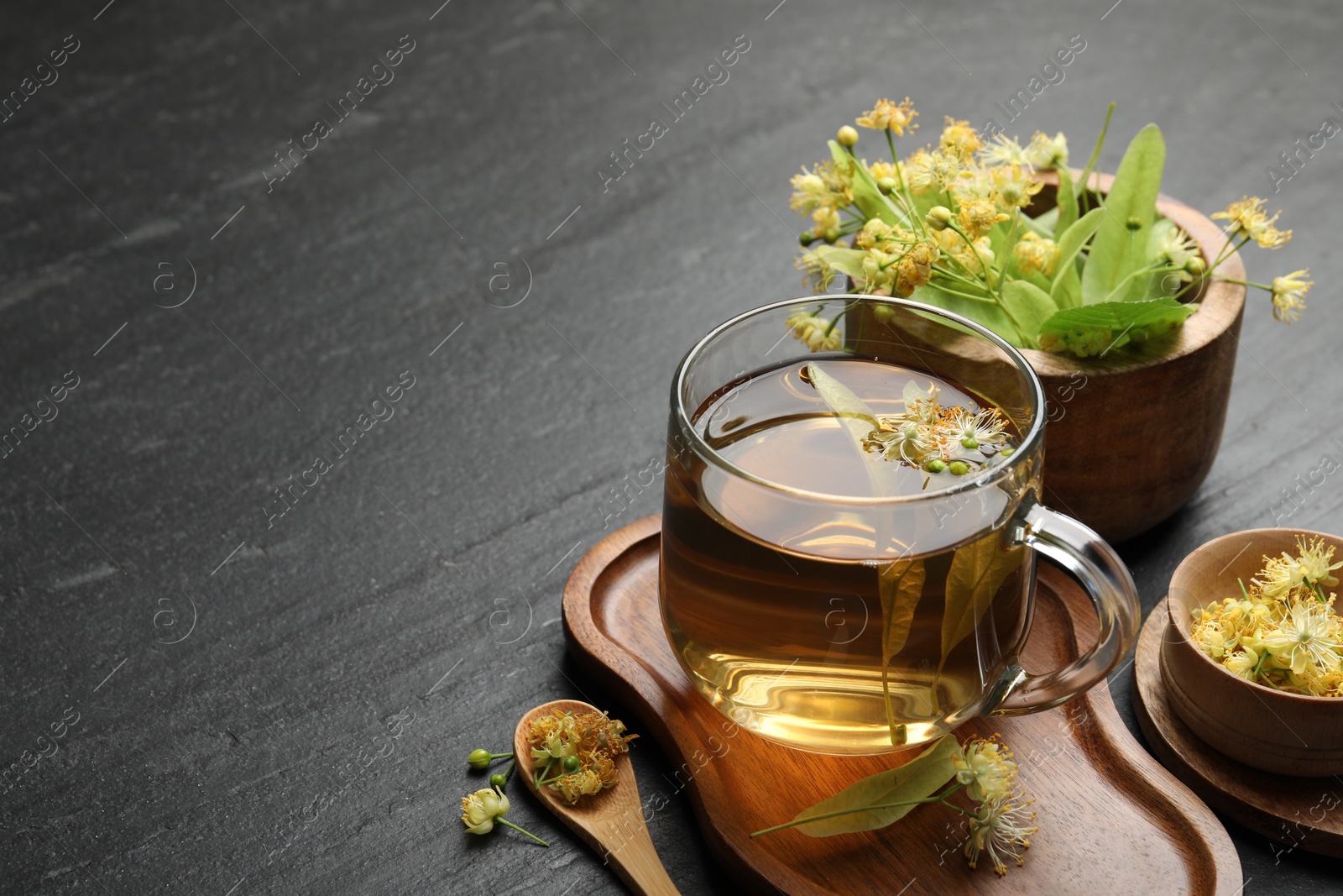 Tasty linden tea in cup, spoon, leaves and flowers on dark textured table, closeup. Space for text Photo of Tasty linden tea in cup, spoon, leaves and flowers on dark textured table, closeup. Space for text