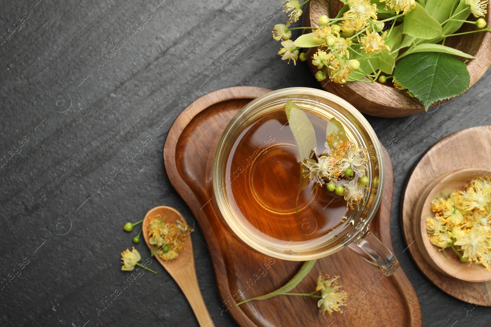 Tasty linden tea in cup, spoon, leaves and flowers on dark textured table, flat lay. Space for text Photo of Tasty linden tea in cup, spoon, leaves and flowers on dark textured table, flat lay. Space for text