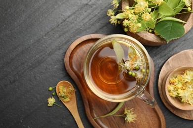 Photo of Tasty linden tea in cup, spoon, leaves and flowers on dark textured table, flat lay. Space for text