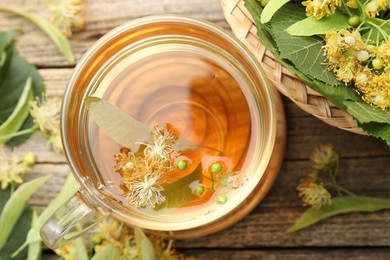 Photo of Tasty linden tea in cup, leaves and flowers on wooden table, flat lay