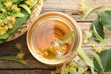 Photo of Tasty linden tea in cup, leaves and flowers on wooden table, flat lay