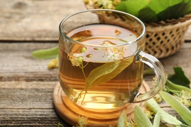 Photo of Tasty linden tea in cup, leaves and flowers on wooden table, closeup