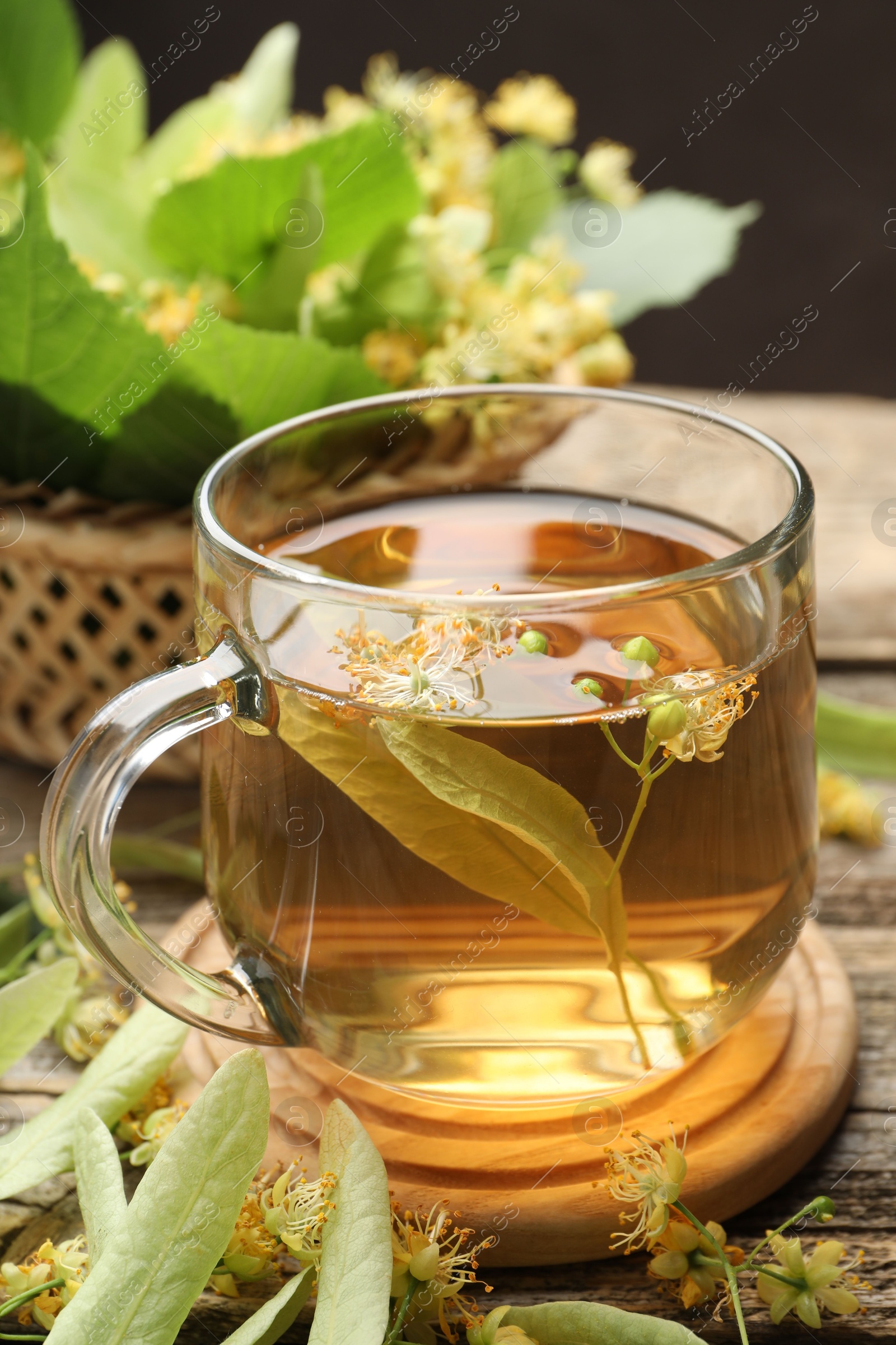 Tasty linden tea in cup, leaves and flowers on wooden table against dark background, closeup Photo of Tasty linden tea in cup, leaves and flowers on wooden table against dark background, closeup