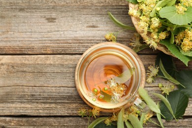 Photo of Tasty linden tea in cup, leaves and flowers on wooden table, flat lay. Space for text
