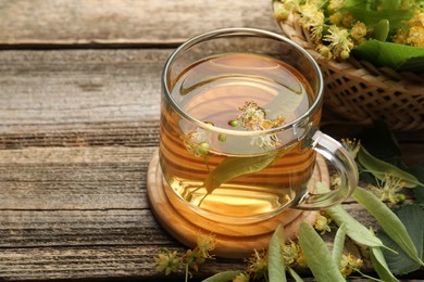Photo of Tasty linden tea in cup, leaves and flowers on wooden table, closeup. Space for text