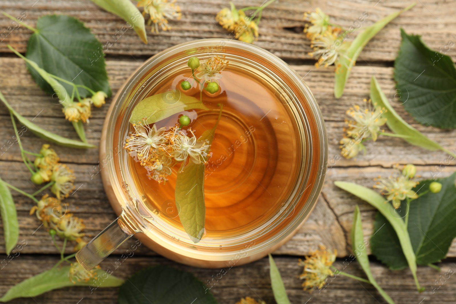Tasty linden tea in cup, leaves and flowers on wooden table, flat lay Photo of Tasty linden tea in cup, leaves and flowers on wooden table, flat lay