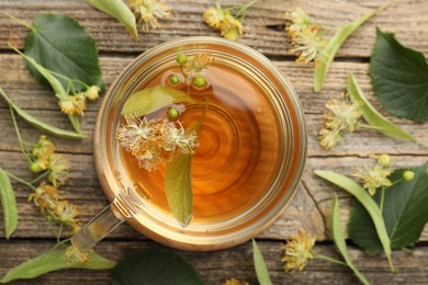 Photo of Tasty linden tea in cup, leaves and flowers on wooden table, flat lay