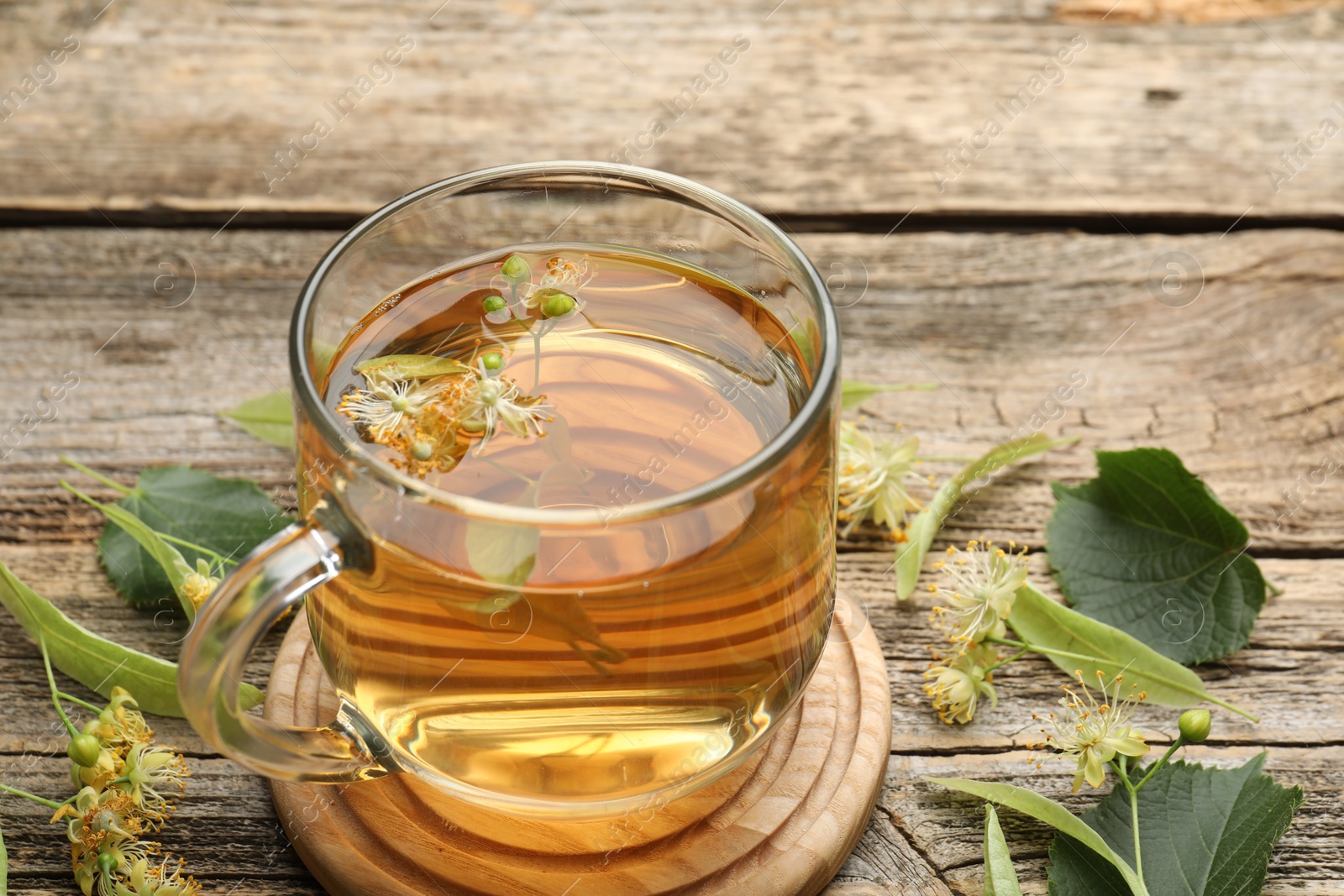 Tasty linden tea in cup, leaves and flowers on wooden table, closeup Photo of Tasty linden tea in cup, leaves and flowers on wooden table, closeup