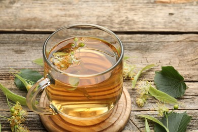 Photo of Tasty linden tea in cup, leaves and flowers on wooden table, closeup