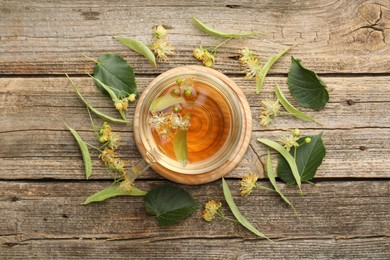 Photo of Tasty linden tea in cup, leaves and flowers on wooden table, flat lay