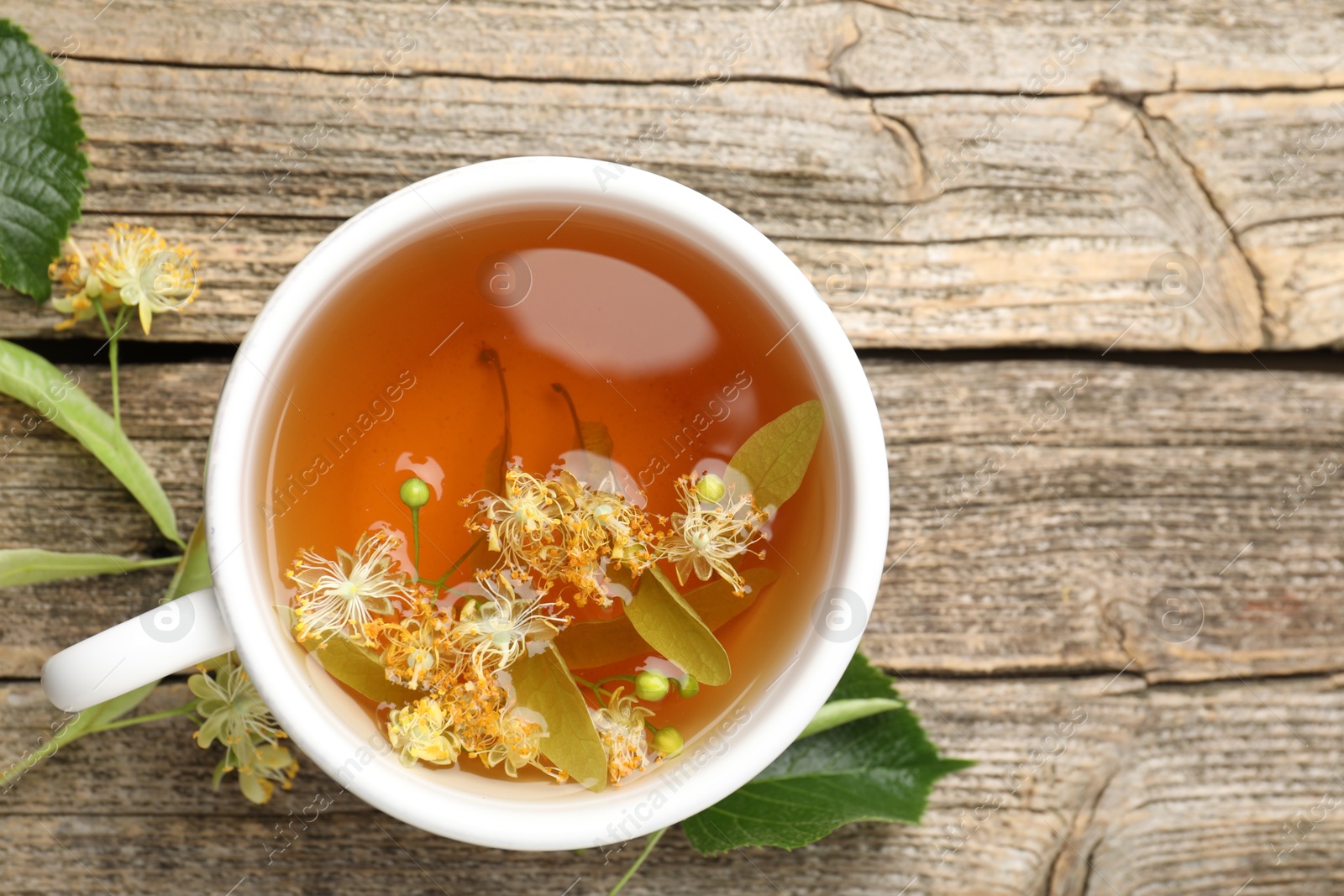 Tasty linden tea in cup, leaves and flowers on wooden table, flat lay Photo of Tasty linden tea in cup, leaves and flowers on wooden table, flat lay