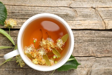Photo of Tasty linden tea in cup, leaves and flowers on wooden table, flat lay