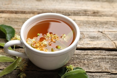 Photo of Tasty linden tea in cup, leaves and flowers on wooden table, closeup
