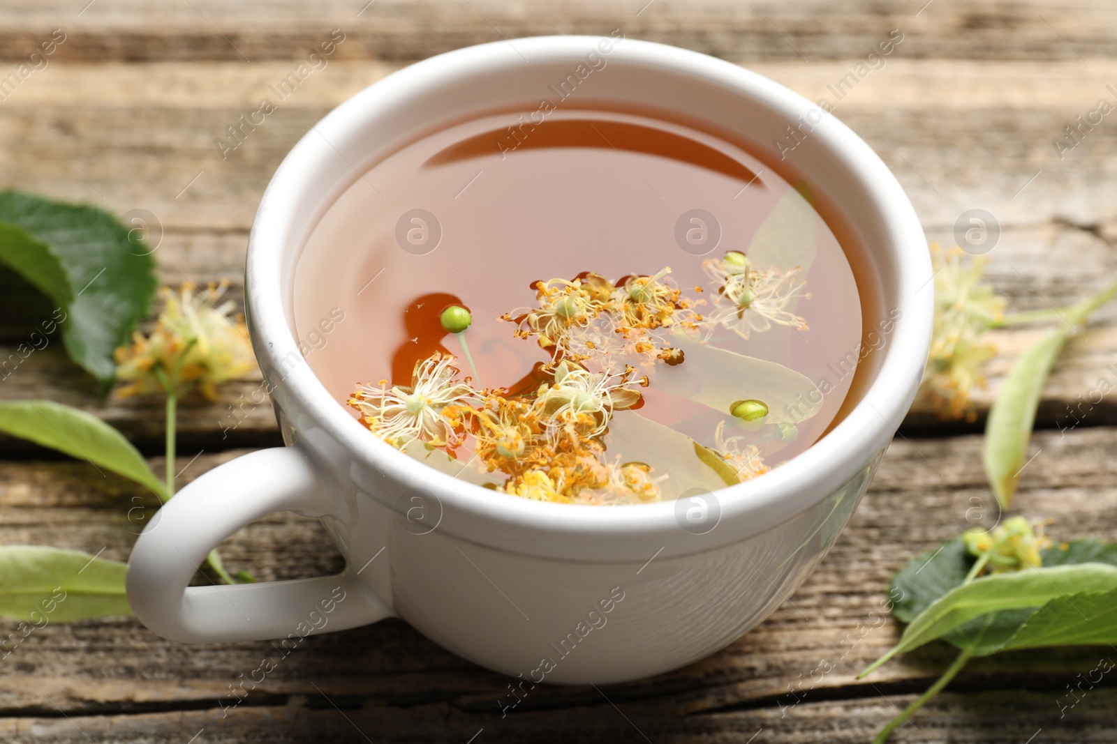 Tasty linden tea in cup, leaves and flowers on wooden table, closeup Photo of Tasty linden tea in cup, leaves and flowers on wooden table, closeup