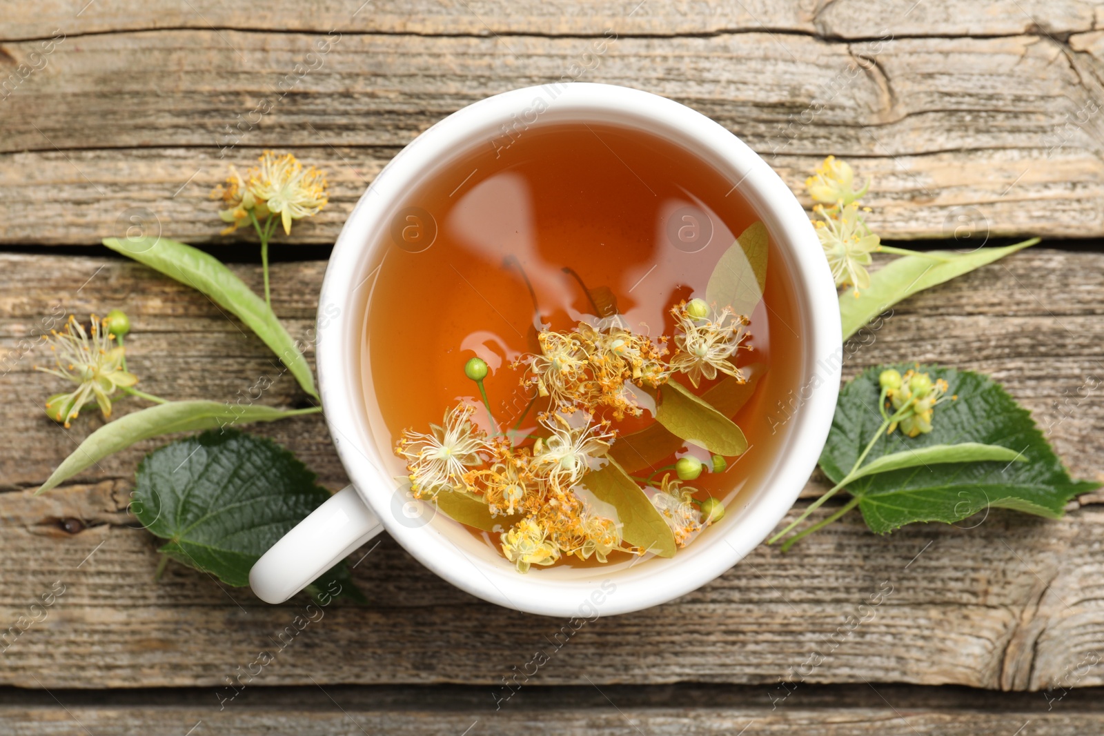 Tasty linden tea in cup, leaves and flowers on wooden table, flat lay Photo of Tasty linden tea in cup, leaves and flowers on wooden table, flat lay
