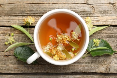 Photo of Tasty linden tea in cup, leaves and flowers on wooden table, flat lay