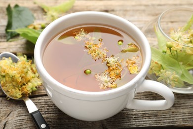 Photo of Tasty linden tea in cup, leaves and flowers on wooden table, closeup