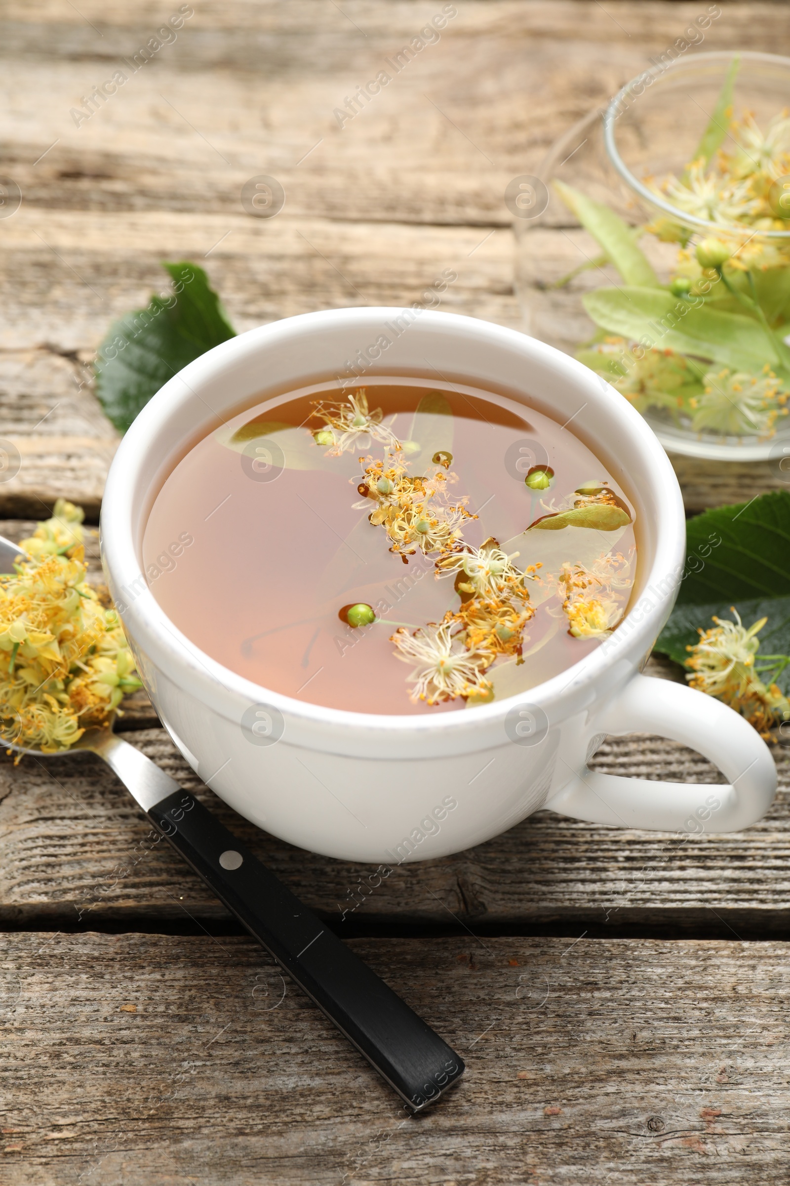 Tasty linden tea in cup, spoon, leaves and flowers on wooden table, closeup Photo of Tasty linden tea in cup, spoon, leaves and flowers on wooden table, closeup