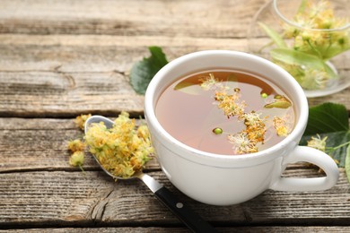 Photo of Tasty linden tea in cup, spoon, leaves and flowers on wooden table, closeup