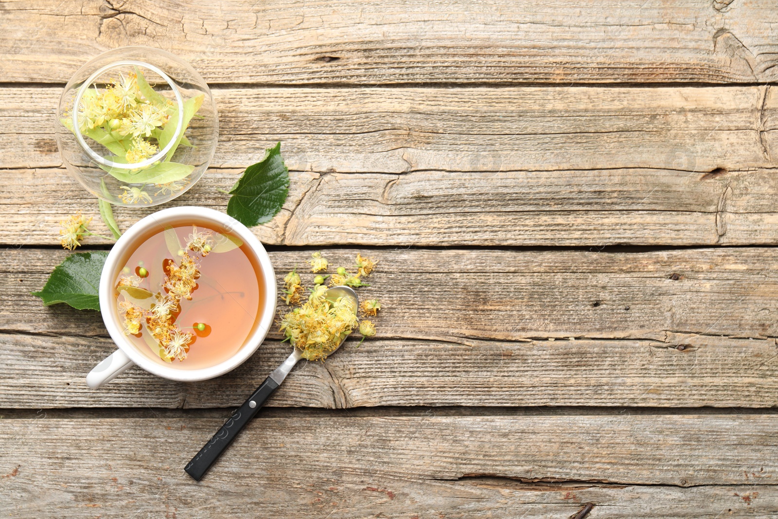 Tasty linden tea in cup, leaves and flowers on wooden table, flat lay. Space for text Photo of Tasty linden tea in cup, leaves and flowers on wooden table, flat lay. Space for text