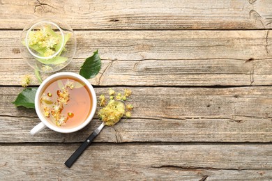 Photo of Tasty linden tea in cup, leaves and flowers on wooden table, flat lay. Space for text
