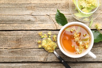 Photo of Tasty linden tea in cup, leaves and flowers on wooden table, flat lay. Space for text