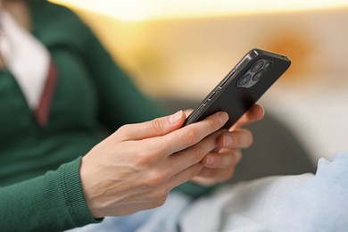 Photo of Woman using modern smartphone on sofa at home, closeup