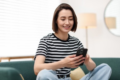 Photo of Woman using modern smartphone on sofa at home