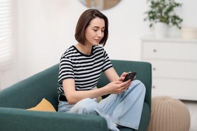 Photo of Woman using modern smartphone on sofa at home