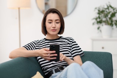 Photo of Woman using modern smartphone on sofa at home