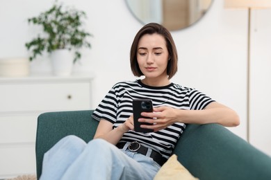 Photo of Woman using modern smartphone on sofa at home