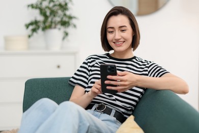 Photo of Woman using modern smartphone on sofa at home. Space for text