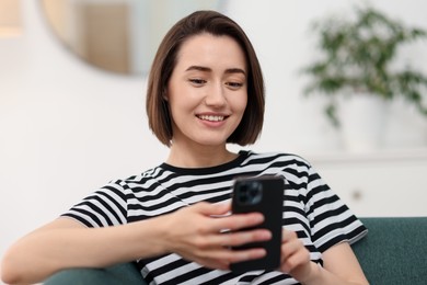 Photo of Woman using modern smartphone on sofa at home