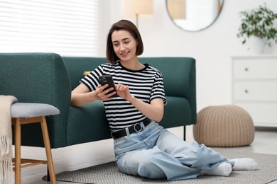 Photo of Woman using modern smartphone on floor at home