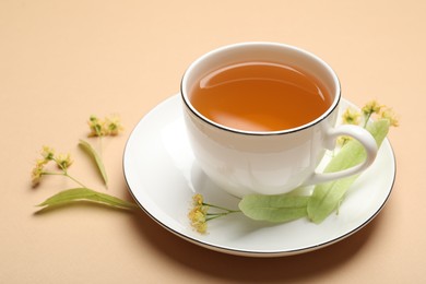 Photo of Tasty linden tea in cup, leaves and flowers on beige table, closeup