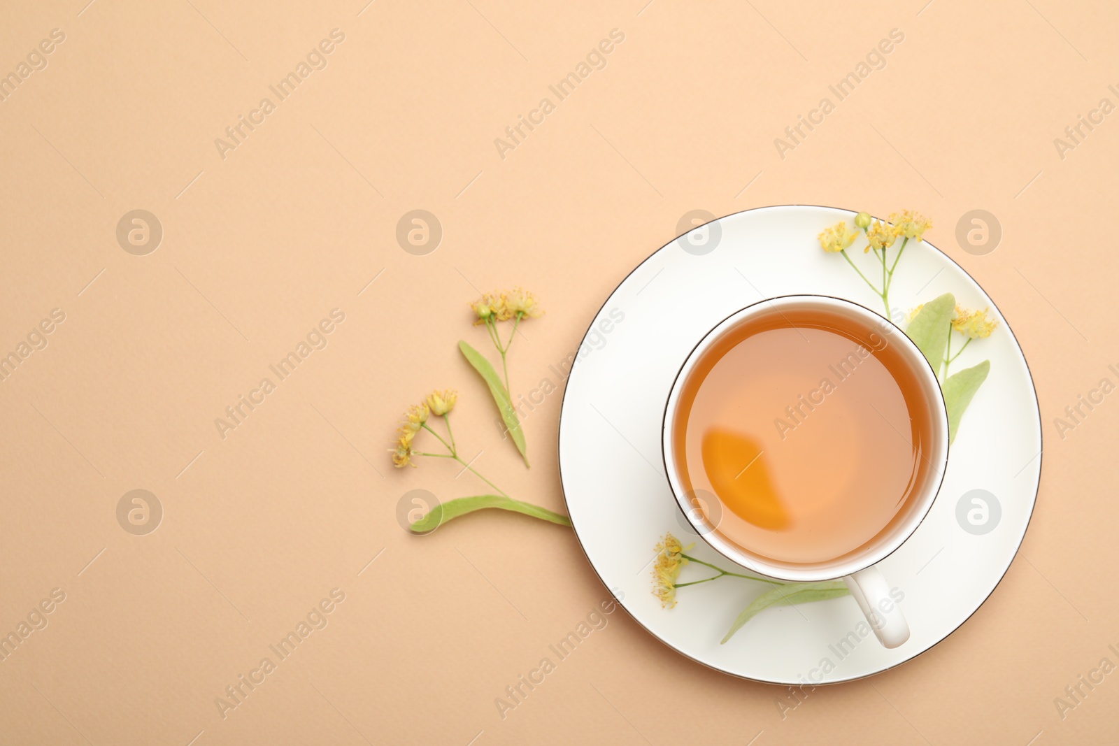 Tasty linden tea in cup, leaves and flowers on beige table, flat lay. Space for text Photo of Tasty linden tea in cup, leaves and flowers on beige table, flat lay. Space for text