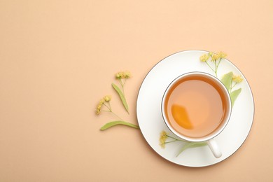 Photo of Tasty linden tea in cup, leaves and flowers on beige table, flat lay. Space for text