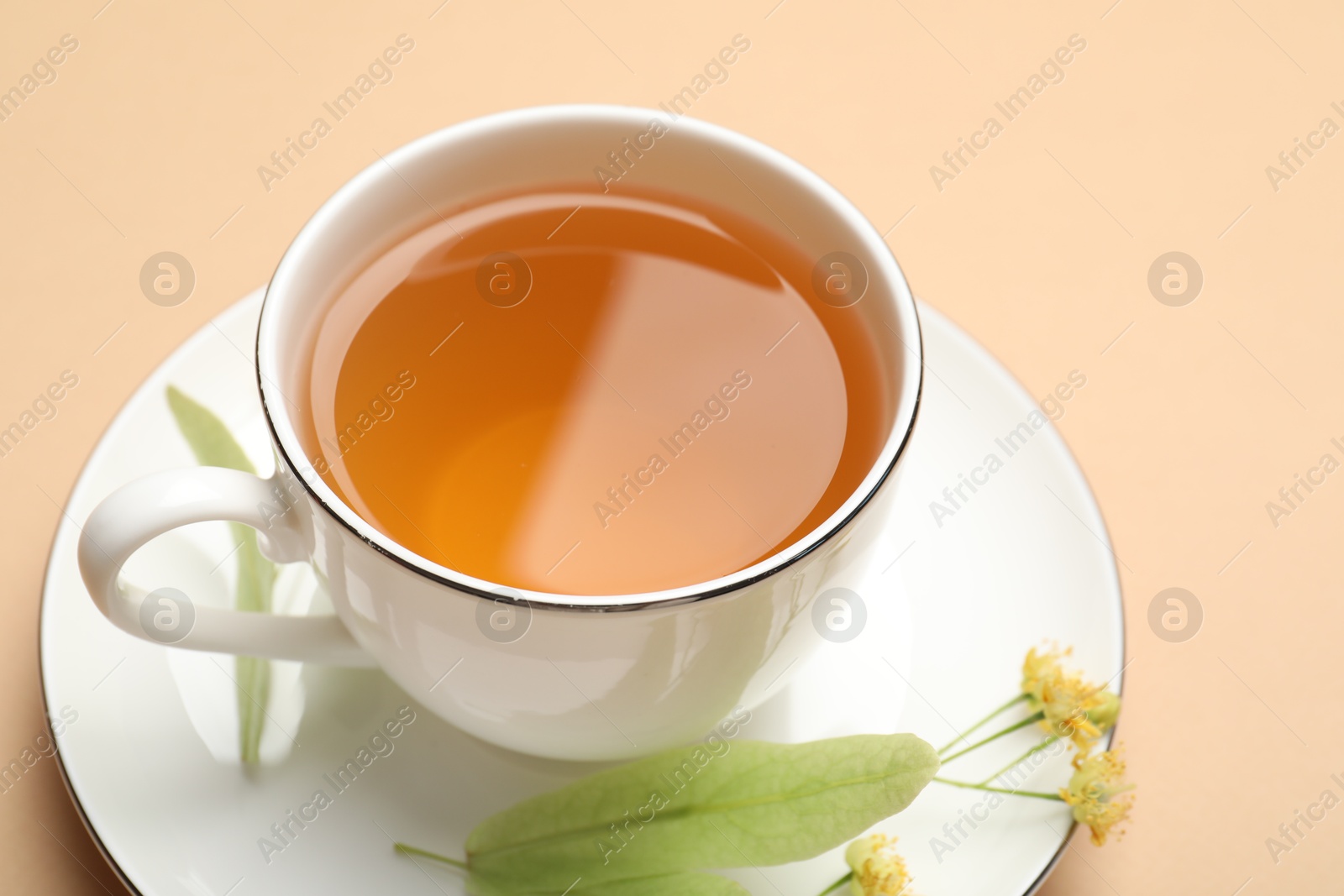 Tasty linden tea in cup, leaves and flowers on beige table, closeup Photo of Tasty linden tea in cup, leaves and flowers on beige table, closeup