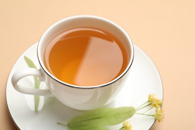 Photo of Tasty linden tea in cup, leaves and flowers on beige table, closeup