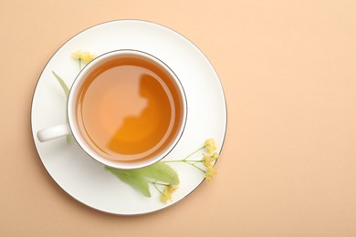 Photo of Tasty linden tea in cup, leaves and flowers on beige table, top view. Space for text