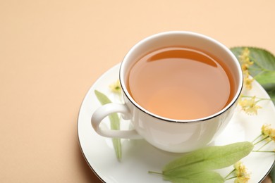 Photo of Tasty linden tea in cup, leaves and flowers on beige table, closeup. Space for text