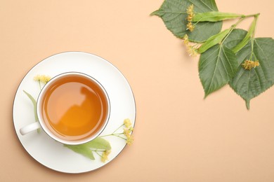 Photo of Tasty linden tea in cup, leaves and flowers on beige table, flat lay. Space for text