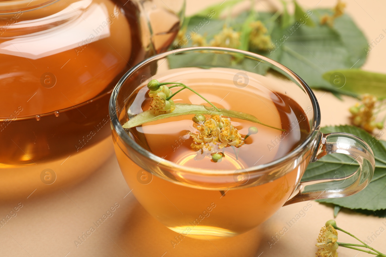 Tasty linden tea in cup, leaves and flowers on beige table, closeup Photo of Tasty linden tea in cup, leaves and flowers on beige table, closeup