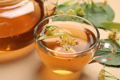 Photo of Tasty linden tea in cup, leaves and flowers on beige table, closeup