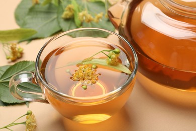 Photo of Tasty linden tea in cup, leaves and flowers on beige table, closeup