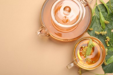 Photo of Tasty linden tea in cup, teapot, leaves and flowers on beige table, flat lay. Space for text