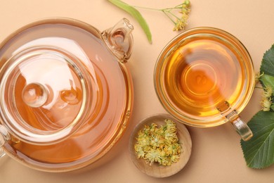 Photo of Tasty linden tea in cup, teapot, leaves and flowers on beige table, flat lay