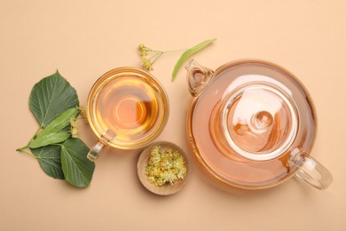 Photo of Tasty linden tea in cup, teapot, leaves and flowers on beige table, flat lay