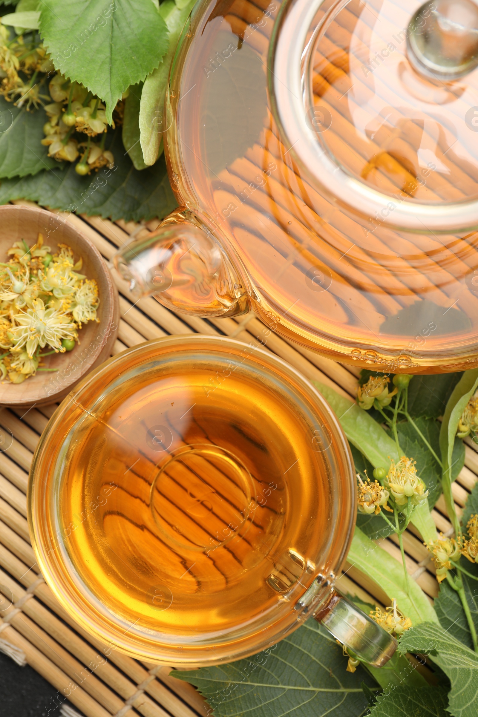 Tasty linden tea in cup, teapot, leaves and flowers on bamboo mat, flat lay Photo of Tasty linden tea in cup, teapot, leaves and flowers on bamboo mat, flat lay